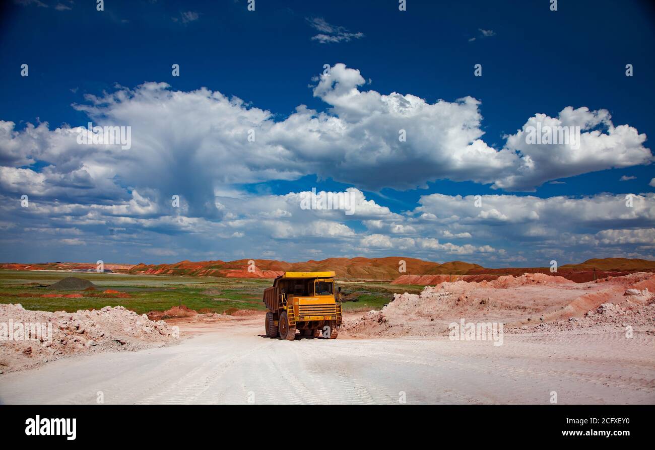 Cava di minerale di alluminio (miniera di bauxite). Estrazione a taglio aperto. Dumper da cava BELAZ su strada bianca e cielo blu con sfondo nuvoloso. Foto Stock