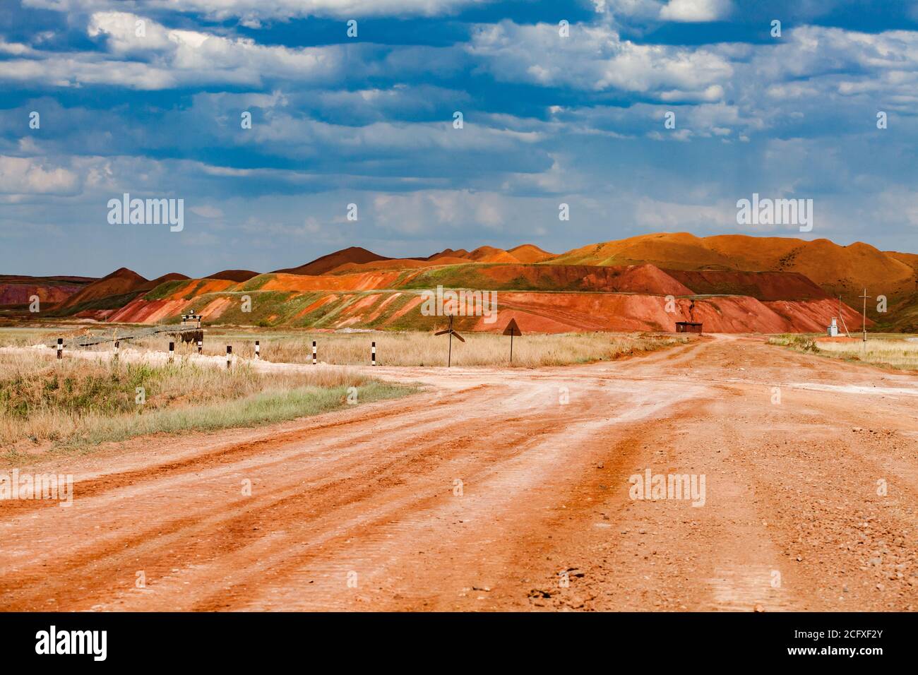 Paesaggio della miniera di bauxite (cava di alluminio). Terra di argilla arancione e cielo blu con le nuvole. Scarponi e una strada con cartelli stradali. Cielo blu con clou Foto Stock