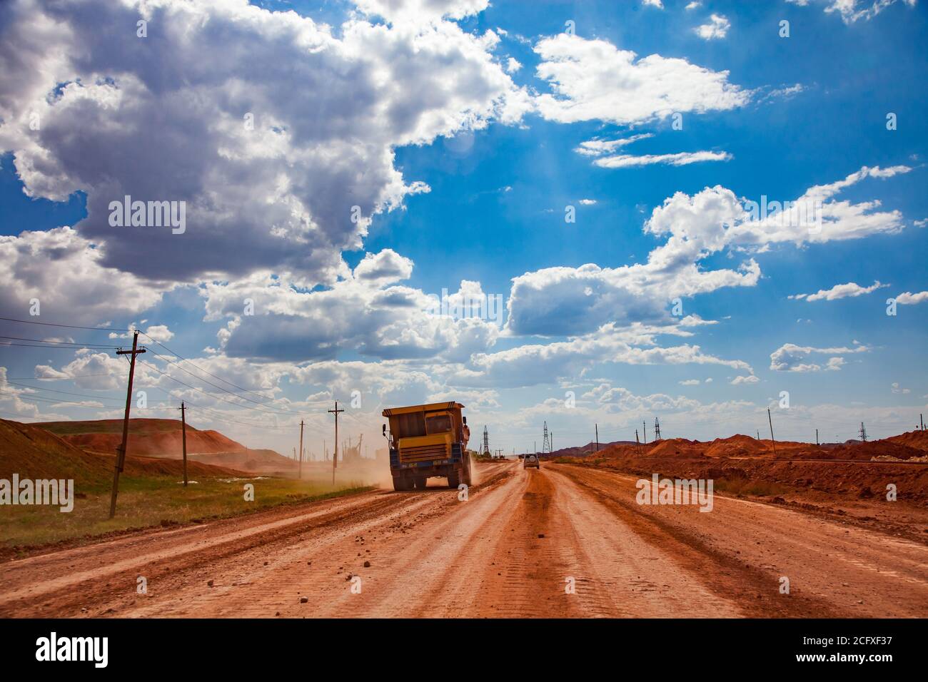 Cava di minerale di alluminio (miniera di bauxite). Scaricano il camion Belaz su una polverosa strada arancione. Cielo blu con sfondo nuvole. Foto Stock