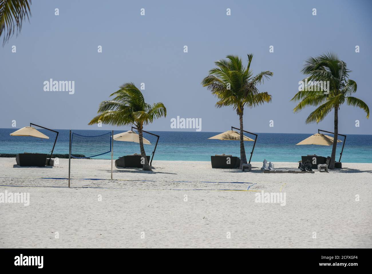 Una fila di lettini ombreggiati e palme fiancheggiano la spiaggia in un resort di lusso nelle Maldive. Foto Stock