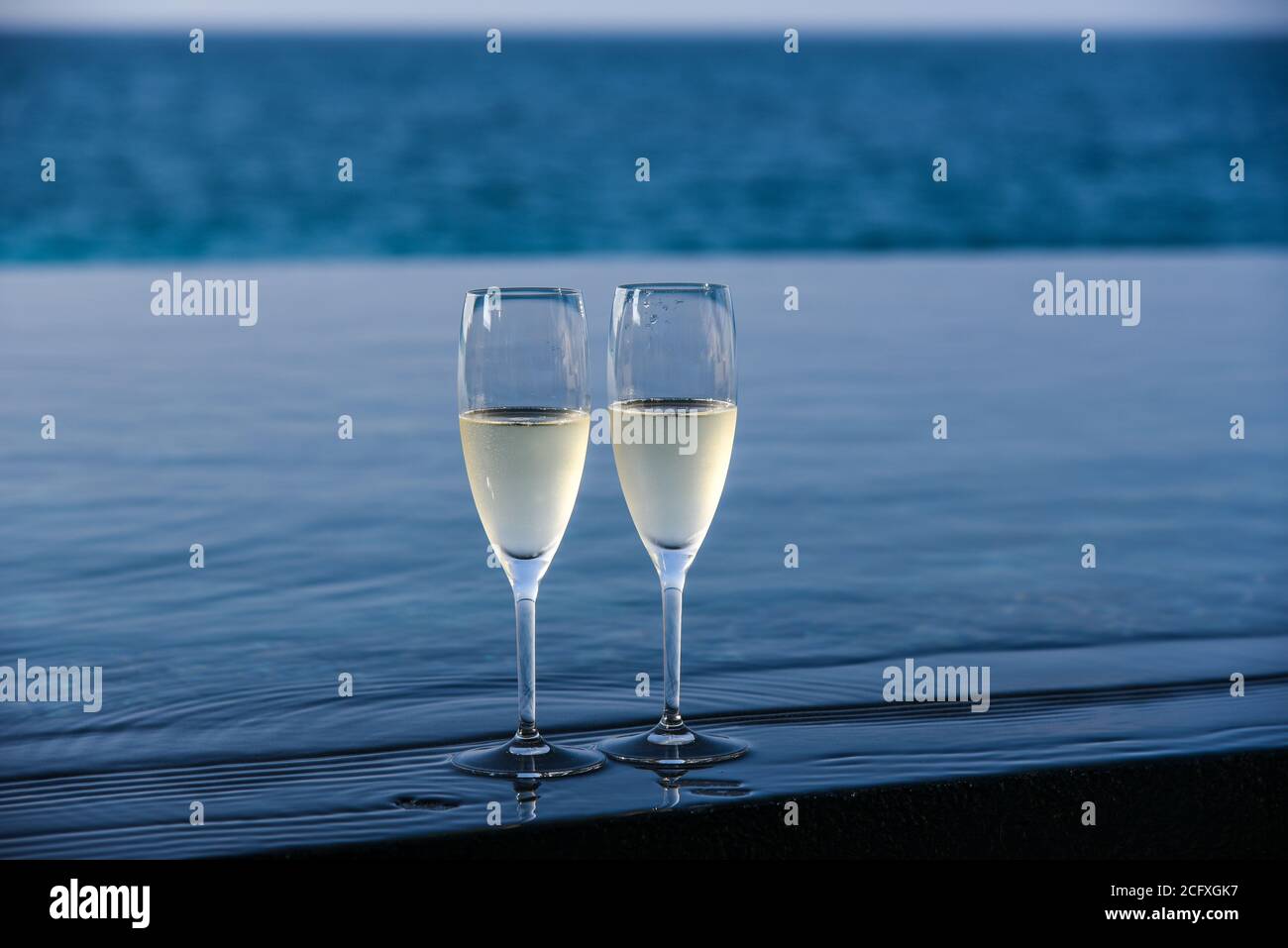 Un paio di flute di champagne sono allestiti sul bordo di una piscina infinity per una coppia da godere sul loro ponte privato in un resort di lusso nelle Maldive. Foto Stock