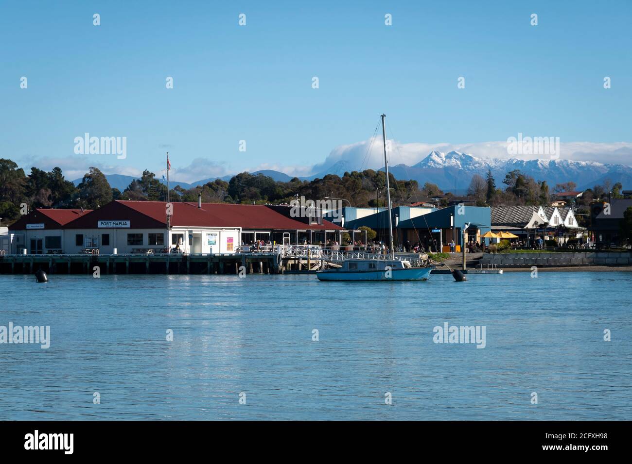 Barche e banchina a Mapua, Nelson, Isola del Sud, Nuova Zelanda. Campo innevato di Mount Arthur in lontananza. Foto Stock