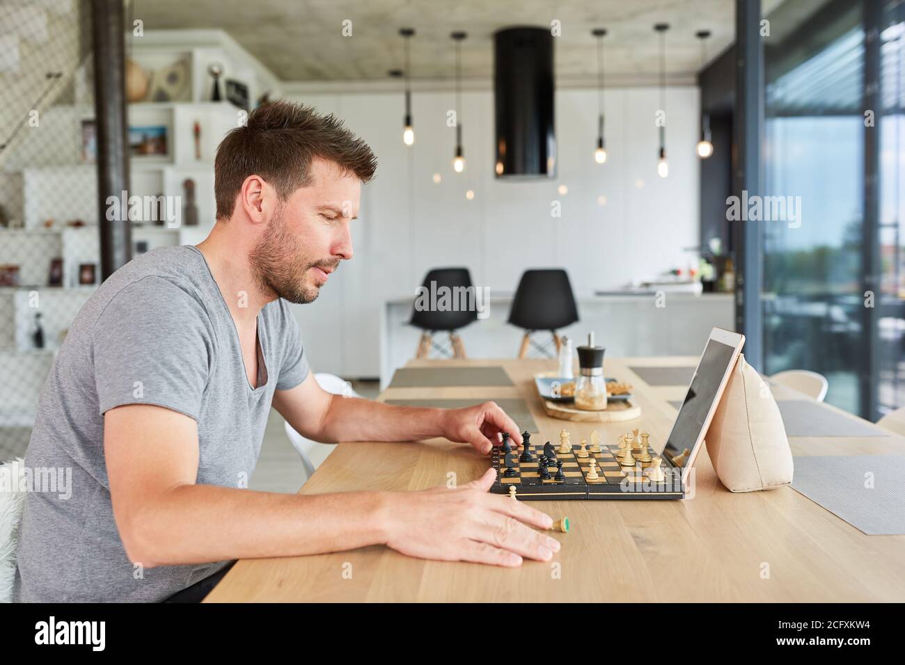 Giovane uomo che gioca a scacchi in video chat online a casa nel soggiorno Foto Stock