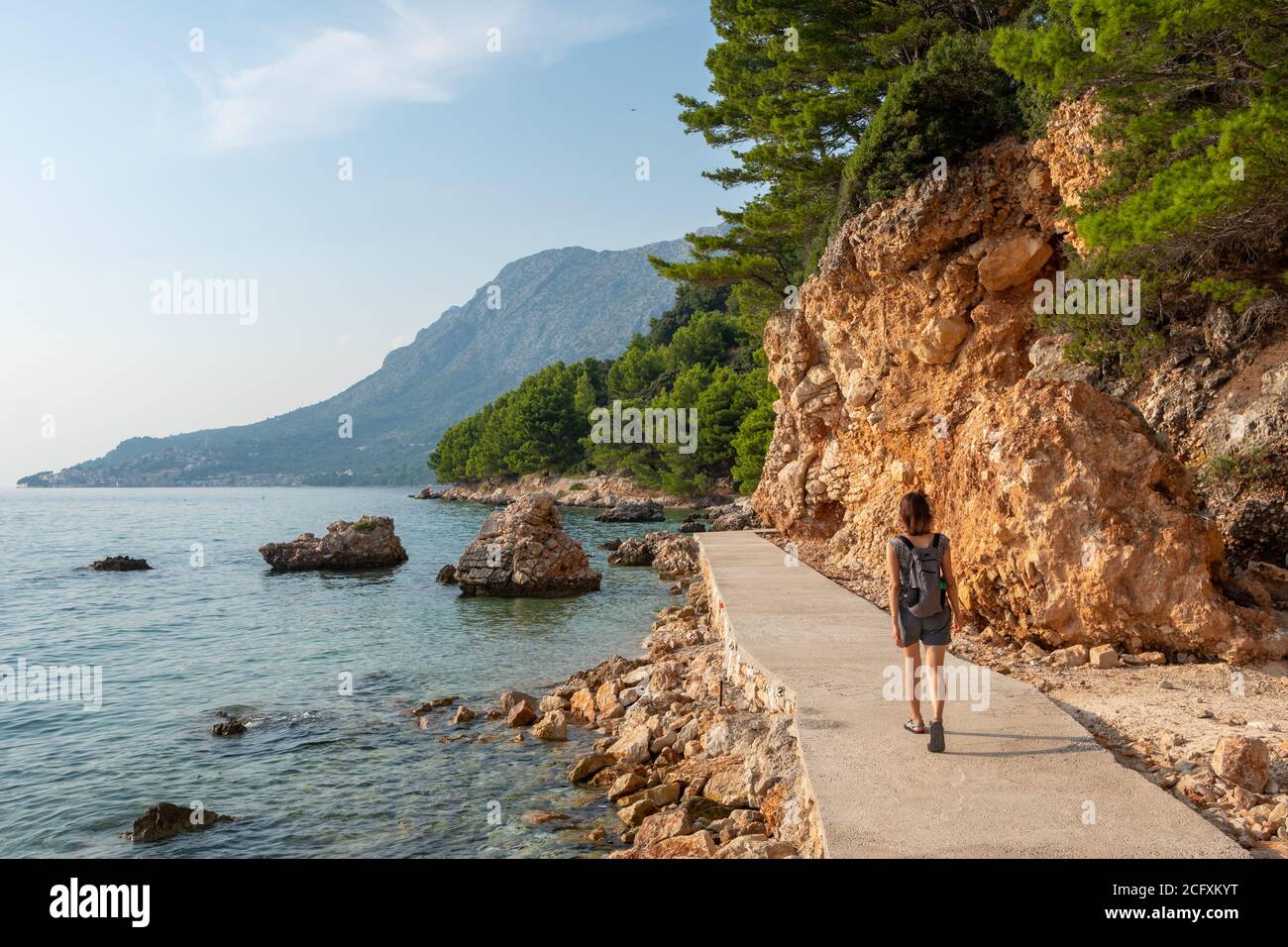 Donna non identificata cammina lungo il percorso turistico lungo la costa adriatica della riviera di Makarska, Croazia Foto Stock