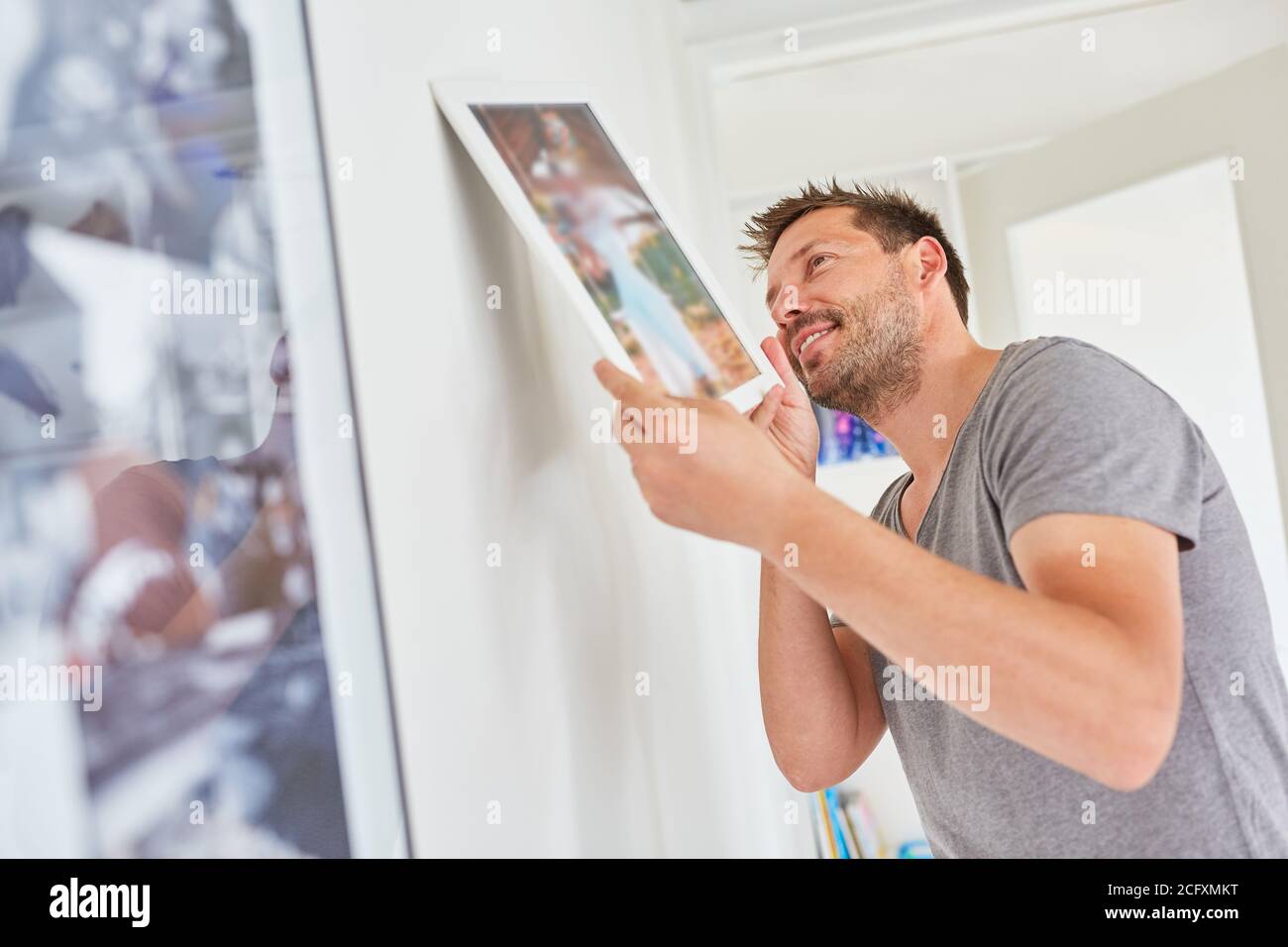 Il giovane collega una cornice con una foto sul parete nel soggiorno Foto Stock