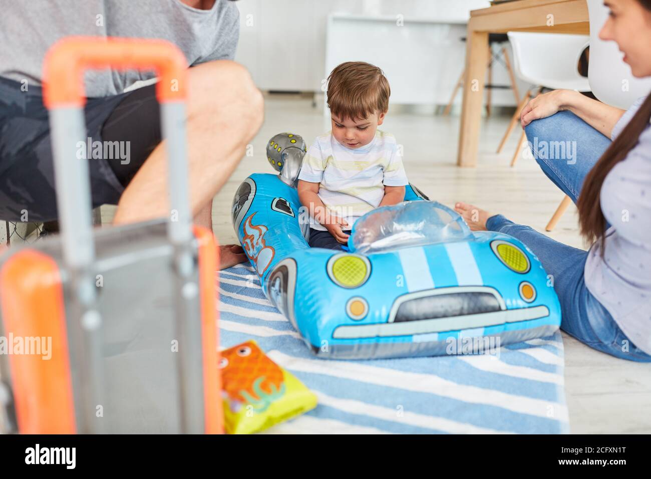 Il bambino guida in auto da corsa come veicolo per bambini nel soggiorno con i genitori Foto Stock