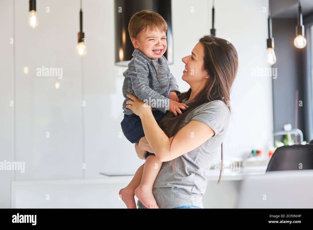 Madre conforta il figlio piangente e lo porta in lei armi nell'appartamento Foto Stock