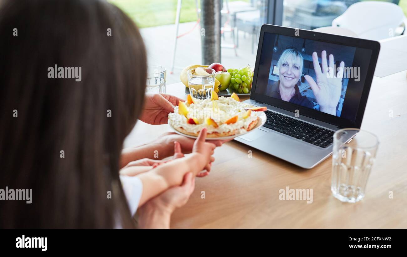 Famiglia con bambino in video chat con nonna che festeggia il compleanno con torta Foto Stock