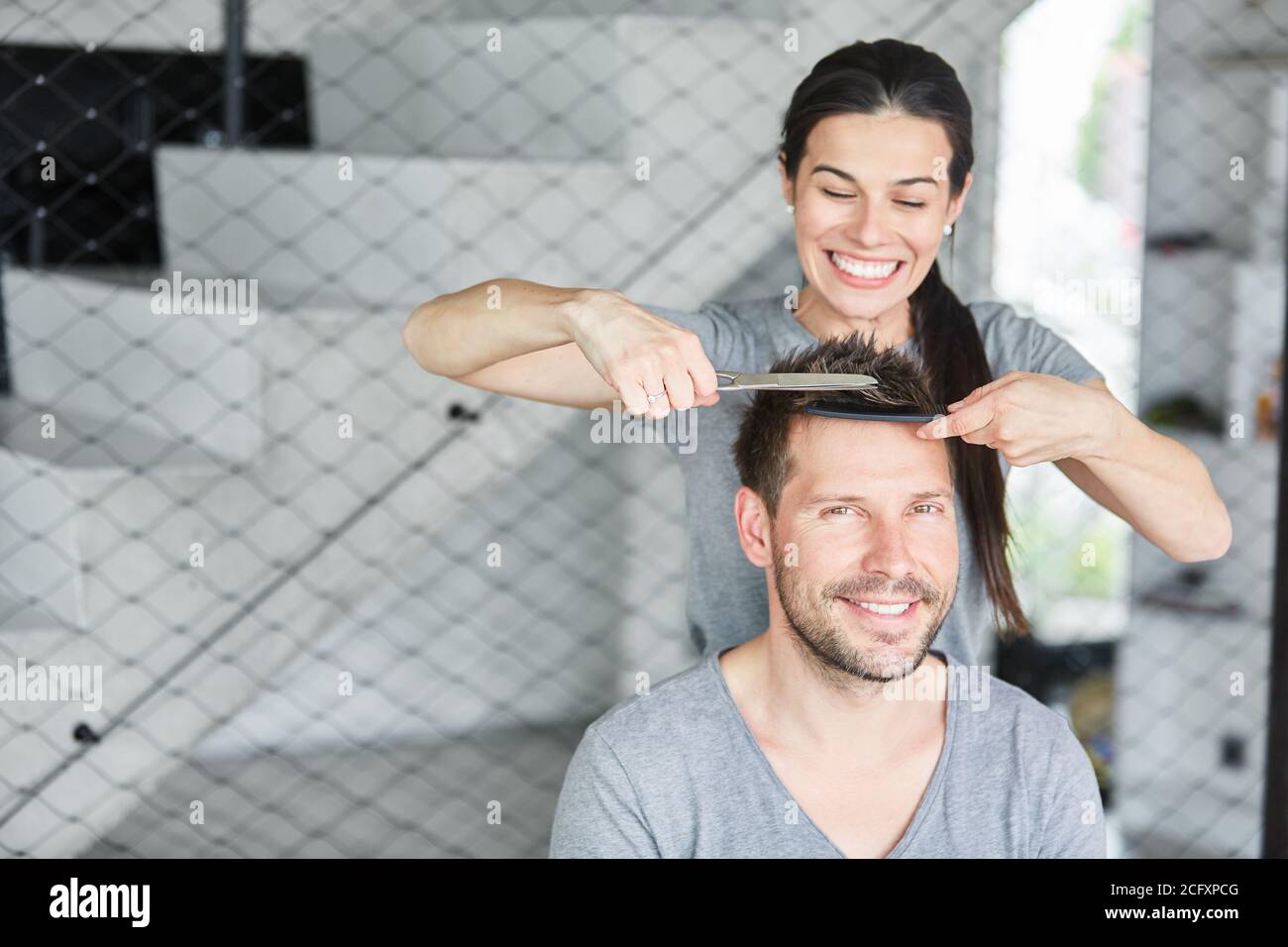 La donna sorridente taglia i capelli del marito con un pettine e forbici Foto Stock