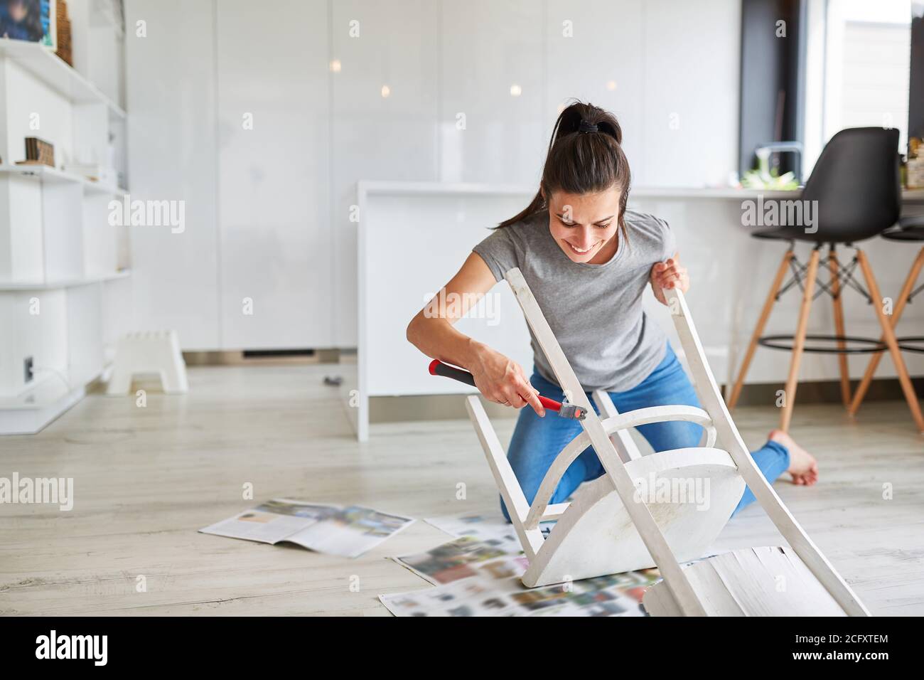 Donna come un handyman a casa che dipinge una sedia o. dipingere come upcycling Foto Stock