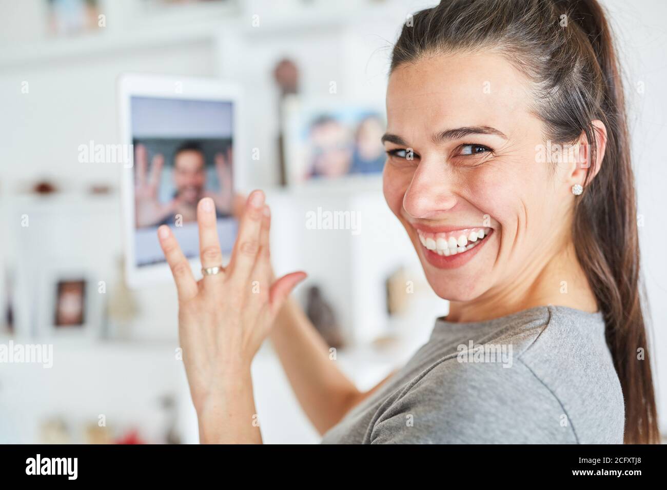 Felice giovane donna che usa il tablet durante la chat video online con il suo partner Foto Stock