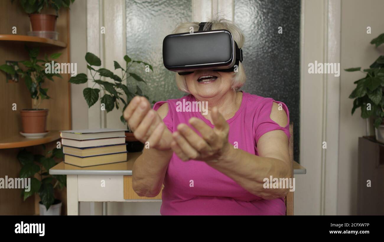 Nonna senior stupita con occhiali per cuffie virtuali che guardano video 3d  straordinari in un casco vr 360 a casa. Tecnologia del futuro. Woman in VR  occhiali giocare, guardando intorno, mostra emozione