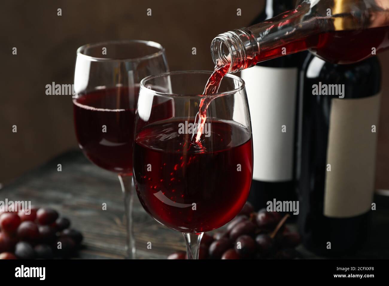 Il vino viene versato da una bottiglia in bicchiere su un tavolo di legno, da vicino Foto Stock