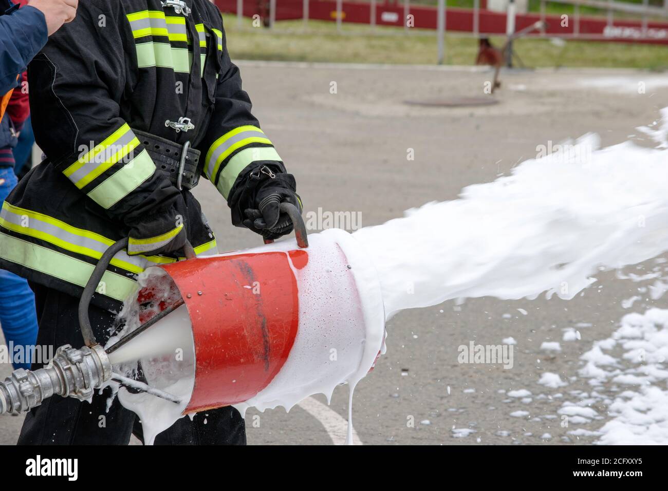 Fornitura di schiuma dal generatore di schiuma, schiuma antincendio vola dal generatore di schiuma, che mantiene il vigile del fuoco in abiti da combattimento Foto Stock