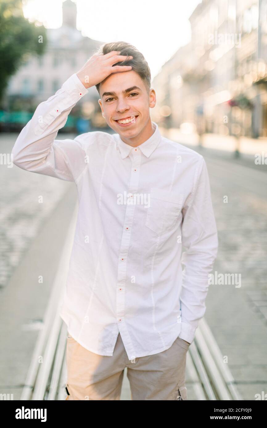 Giovane ed elegante uomo caucasico che indossa camicia bianca e pantaloni  beige, in piedi sulla strada su un bellissimo sfondo di antica città  europea, sorridente Foto stock - Alamy