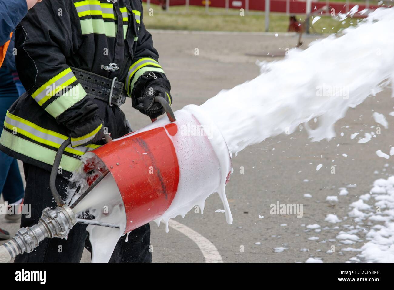 Fornitura di schiuma dal generatore di schiuma, schiuma antincendio vola dal generatore di schiuma, che mantiene il vigile del fuoco in abiti da combattimento Foto Stock
