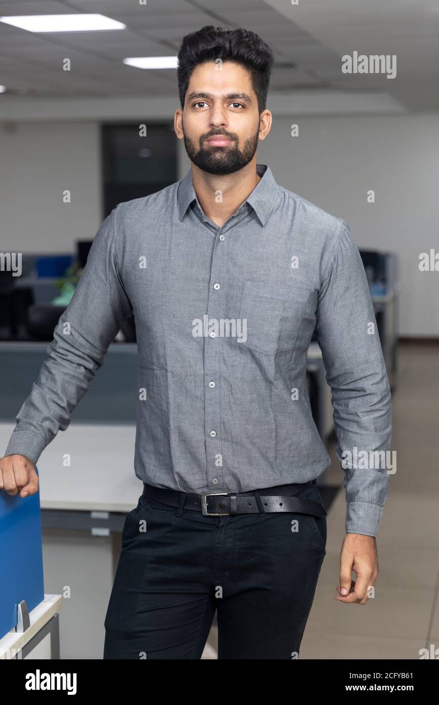 Ritratto di bel giovane uomo d'affari indiano che guarda casualmente nella macchina fotografica. Ambiente aziendale. Foto Stock