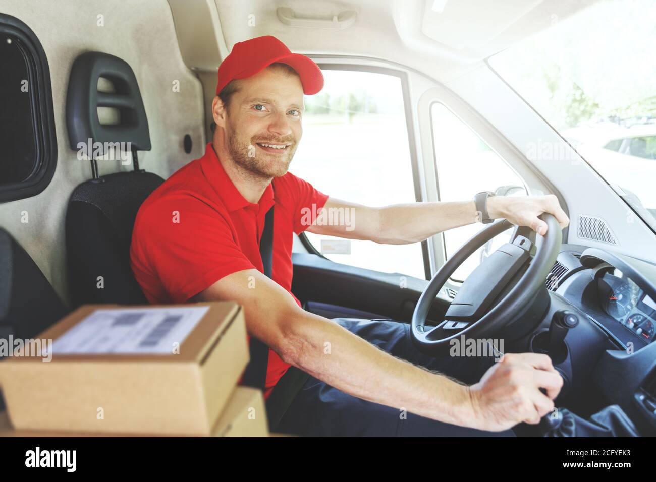 sorridente addetto al servizio di consegna in pulmino rosso uniforme e. consegna dei pacchetti Foto Stock
