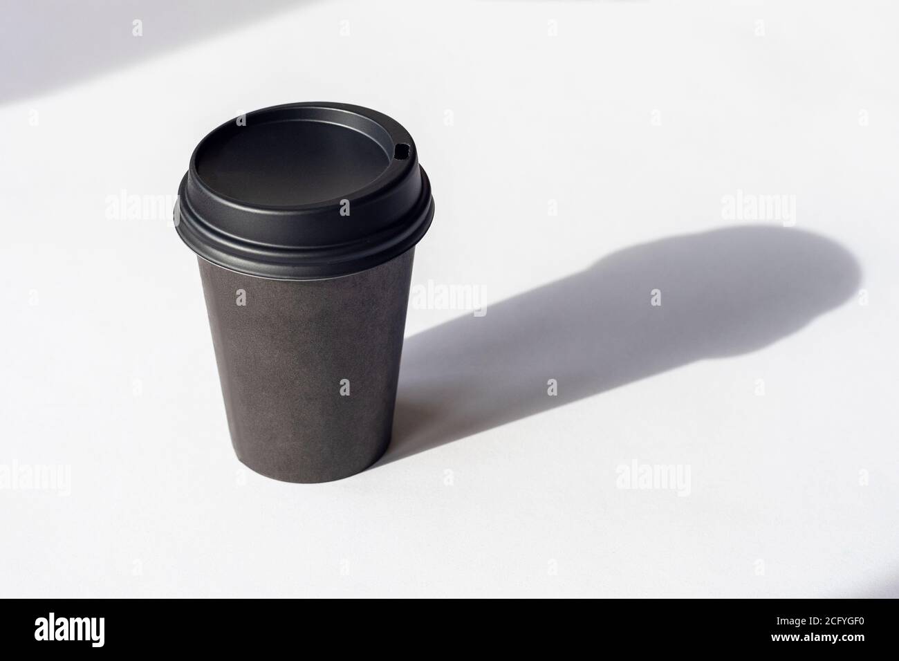Tazza da caffè monouso su tavolo bianco, ombre nitide. Foto Stock