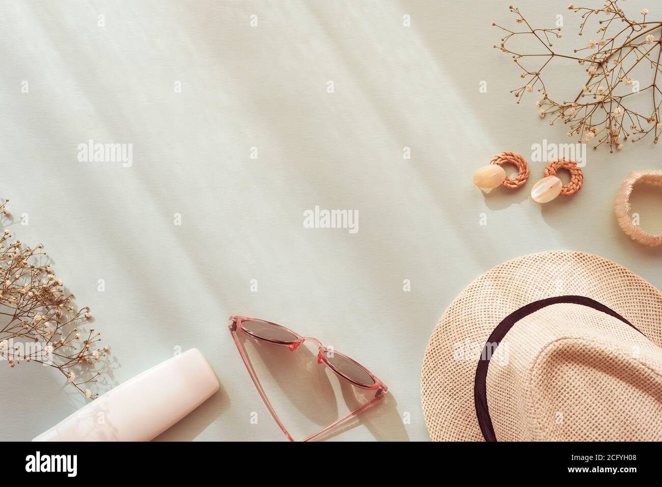 Accessori estivi femminili su sfondo blu. Occhiali da sole, cappello di paglia, orecchini, bracciale, bottiglia cosmetica e pianta gypsophila con ombre. Vista dall'alto, Foto Stock
