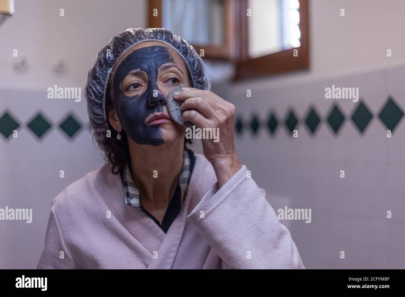 Donna che prende via maschera di fango con spugna Foto Stock