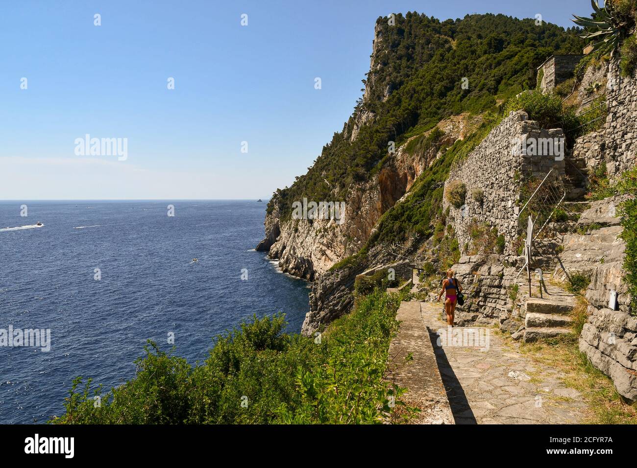 Una ragazza da dietro camminando sul sentiero in pietra della scogliera che domina la riva del mare in estate, Porto Venere, la Spezia, Liguria, Italia Foto Stock