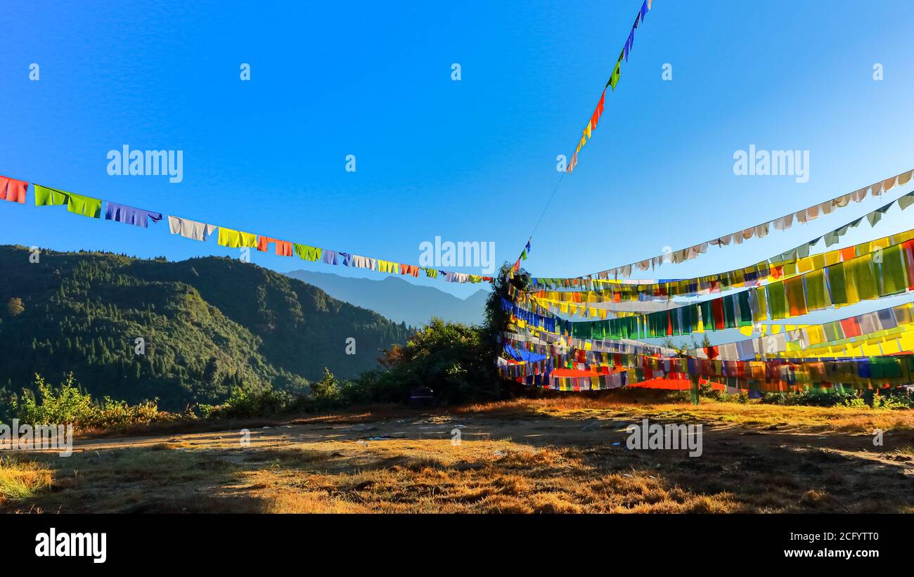 Bandiere colorate di preghiera tibetane contro i raggi del sole di mattina presto che guardano Bella con il paesaggio in Sikkim India Foto Stock