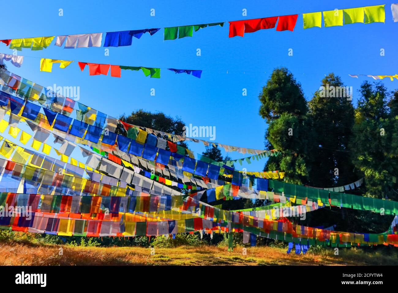 Bandiere colorate di preghiera tibetane contro i raggi del sole di mattina presto che guardano Bella con il paesaggio in Sikkim India Foto Stock