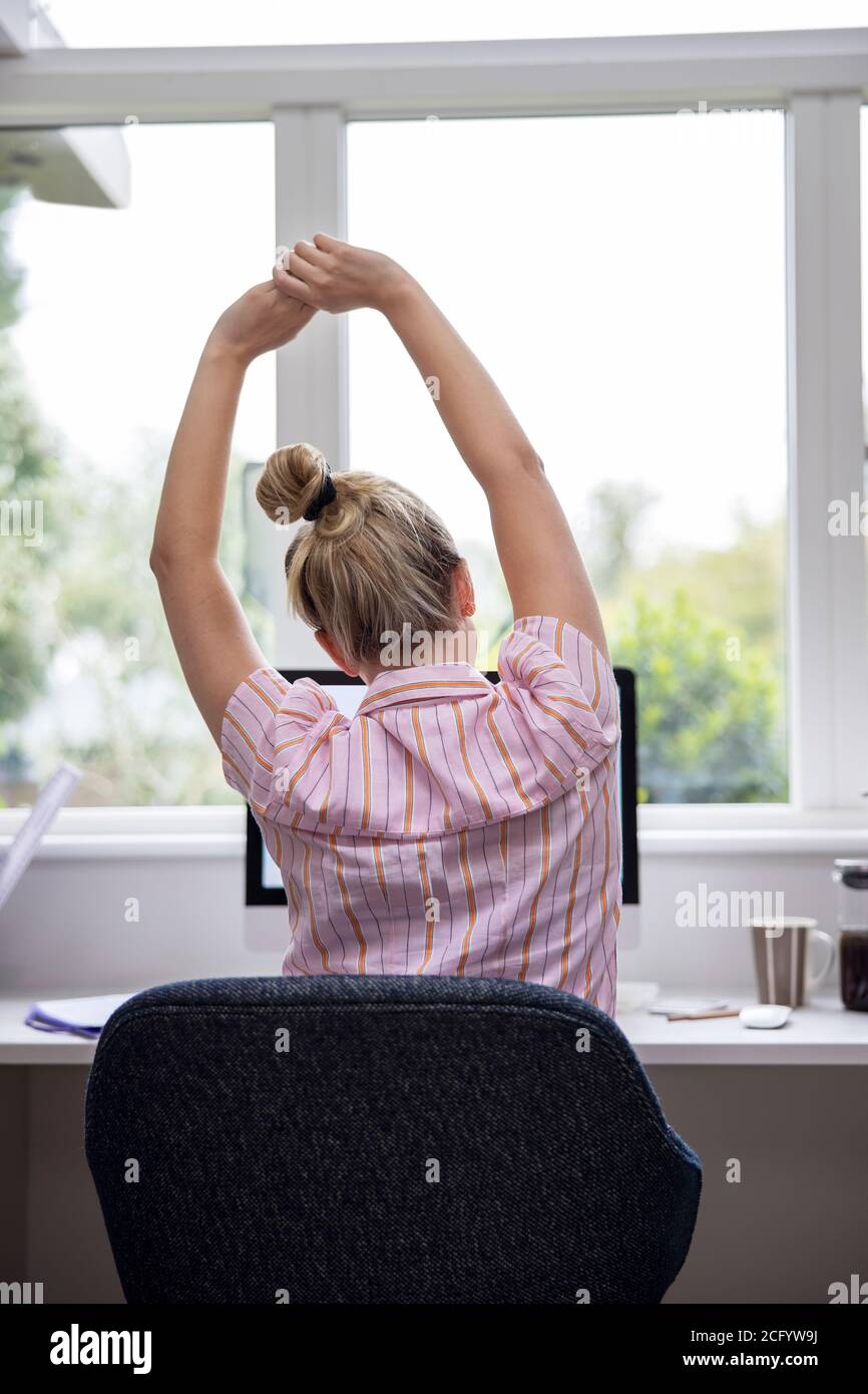 Vista posteriore di Donna che lavora da casa su computer in Home Office stretching alla scrivania Foto Stock