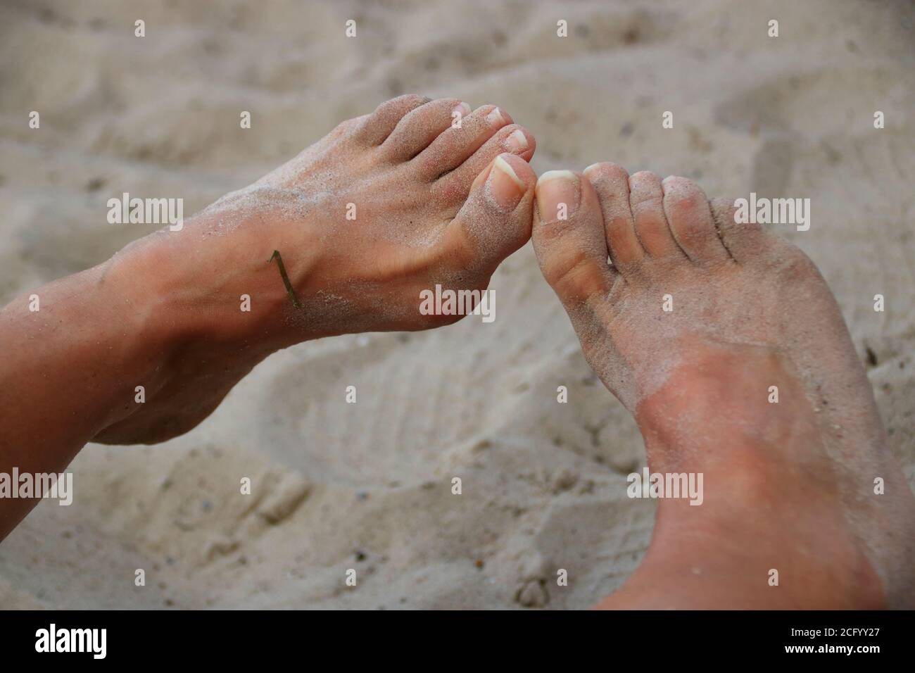 I piedi su una spiaggia di sabbia sono coperti di sabbia Foto Stock