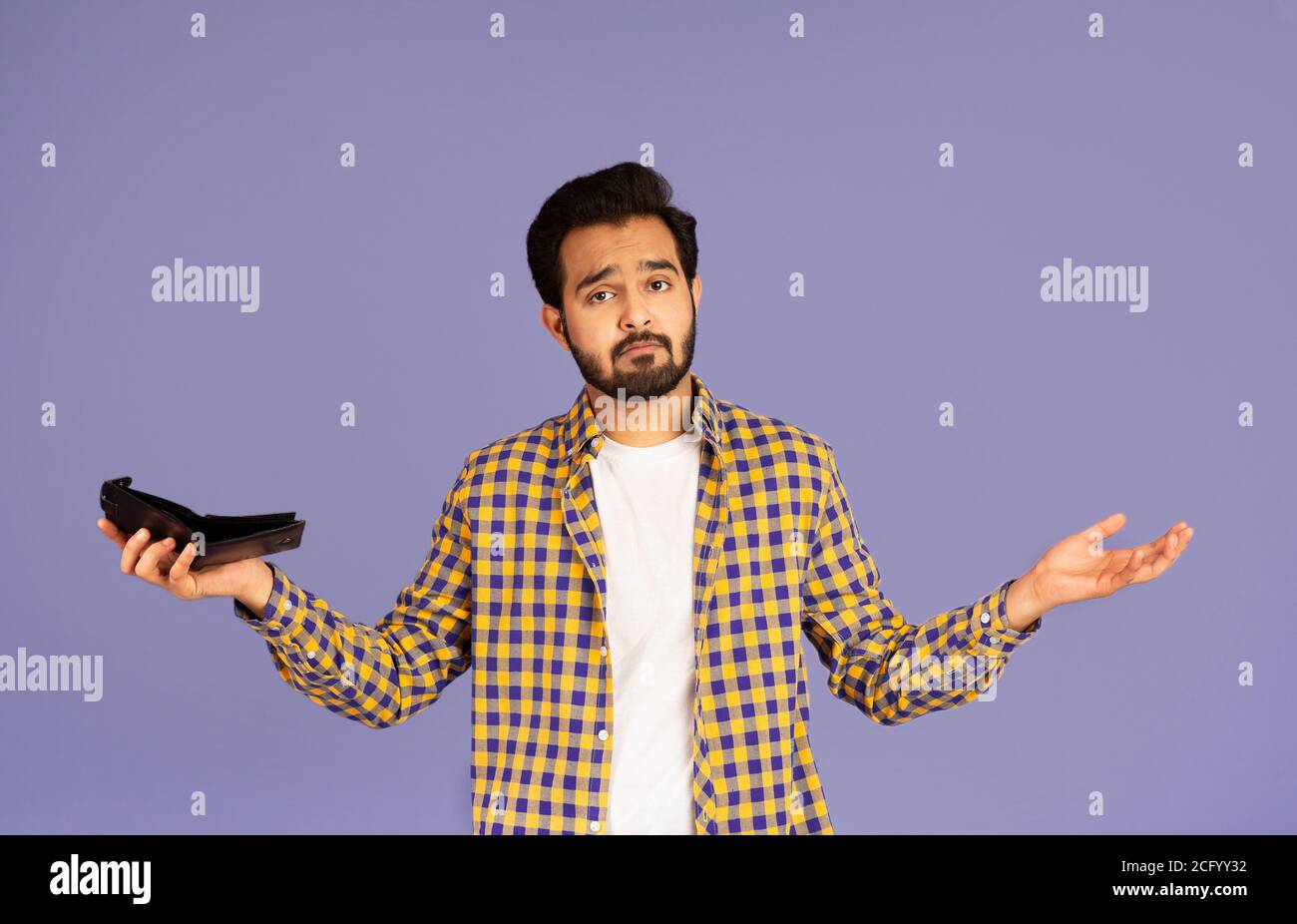 Crisi economica e bancarotta. Un ragazzo indiano sconvolto con un portafoglio vuoto che le spalle si infrangono su sfondo viola Foto Stock