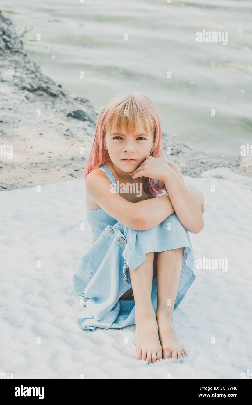 Piccola ragazza affascinante seduta vicino al fiume. Bambina vicino al  fiume su una plaid in un vestito Foto stock - Alamy