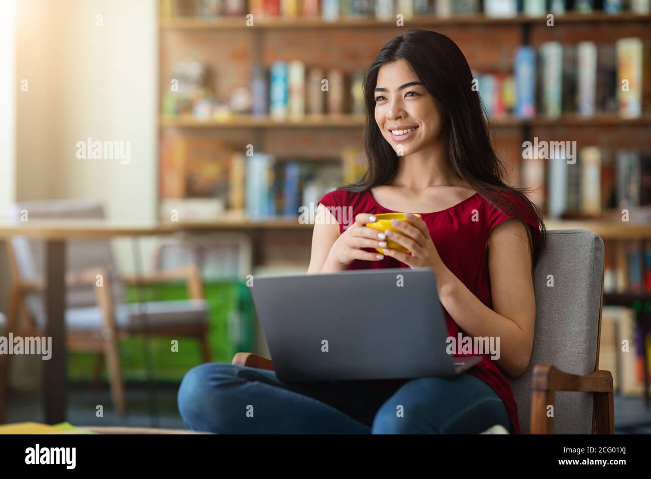Pausa caffè. Ragazza asiatica gustando una bevanda calda mentre si usa il computer portatile al caffè Foto Stock