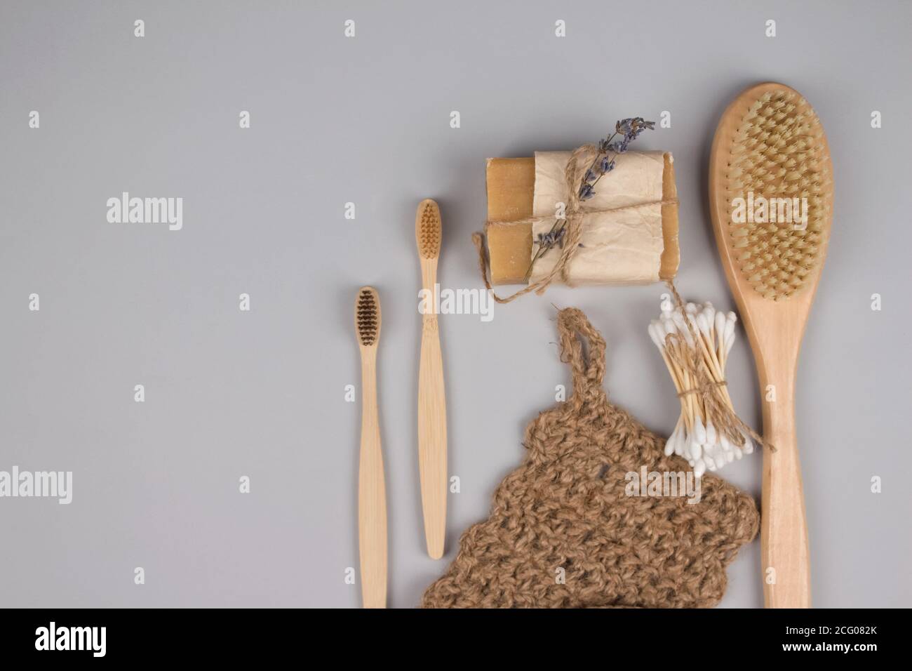 Set di zero rifiuti essenziali bagno su sfondo grigio - spazzolini da denti in bambù, boccioli di cotone, spazzola per il corpo in legno, panno per iuta e sapone organico, asciuga s Foto Stock