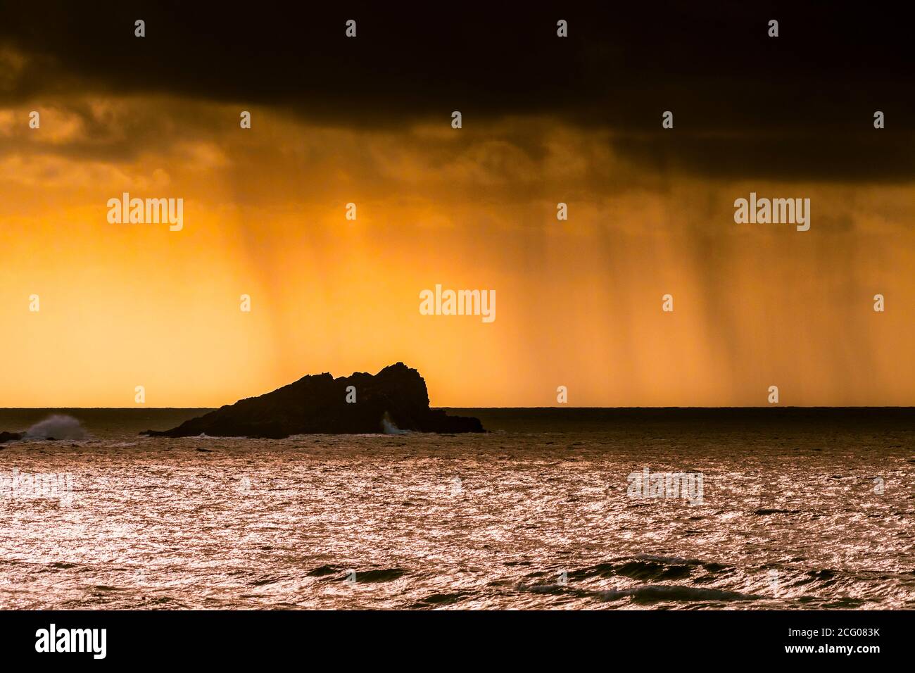 Nuvole di pioggia e uno spettacolare tramonto fiero sull'isola di Goose a Fistral a Newquay in Cornovaglia. Foto Stock