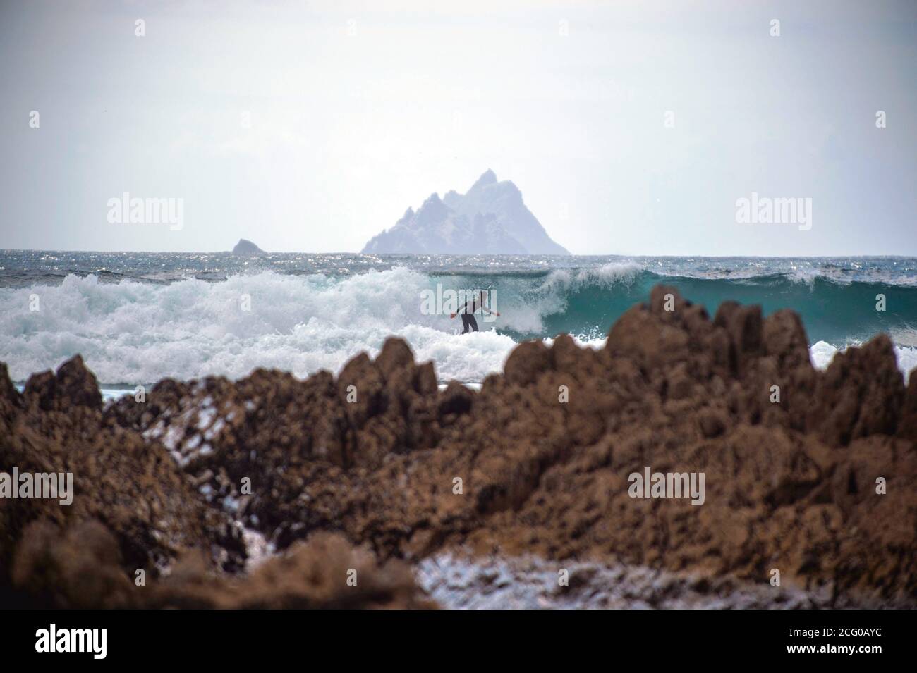 Un surfista corre le onde con le isole Skellig sullo sfondo a St. Finan's Bay a South Kerry, Irlanda. Foto Don MacMonagle Foto Stock