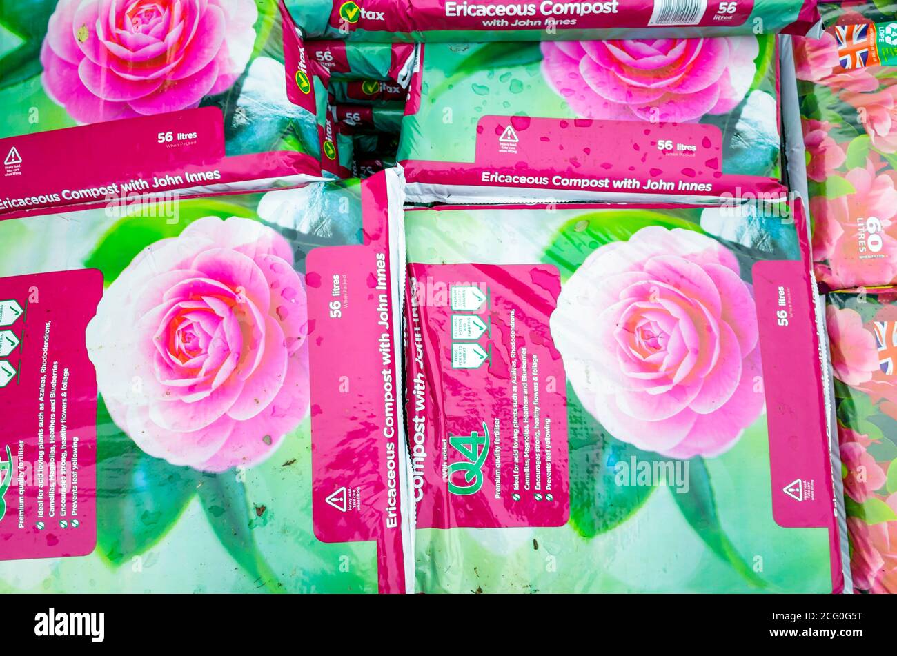 Una pila di sacchetti rosa di composto ericaceo con John Innes in un centro giardino Foto Stock