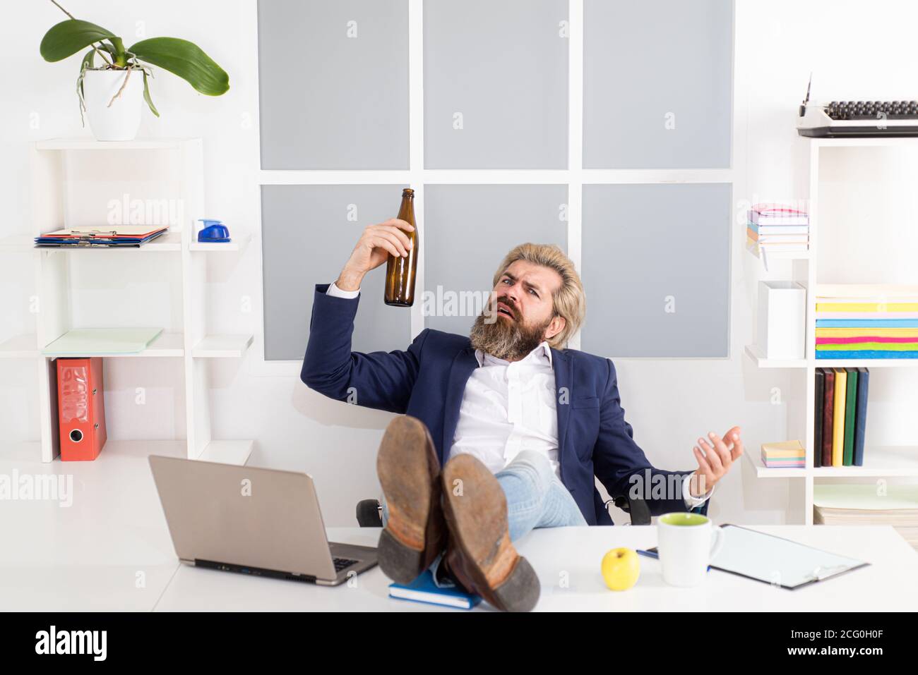 Uomo d'affari che beve dallo stress. Fine della giornata lavorativa. L'uomo d'affari depresso ha problemi sul lavoro, bevendo alcol in ufficio. Foto Stock