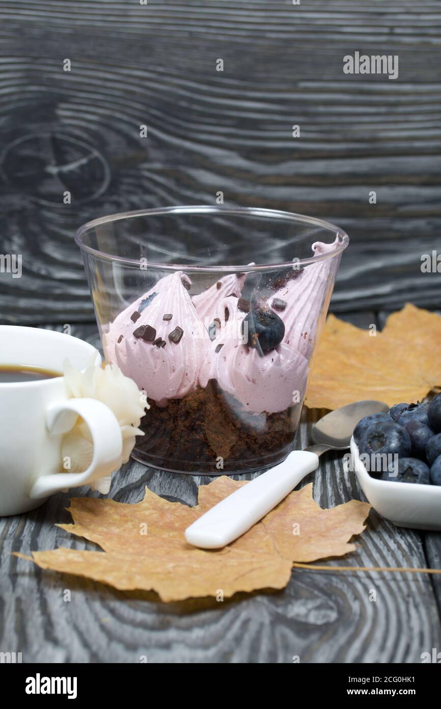 Zephyr in un bicchiere. Con biscotto e mirtilli. Accanto si trova una tazza di caffè e un piatto di mirtilli. Tra le foglie d'acero. Su tavole di pino pai Foto Stock