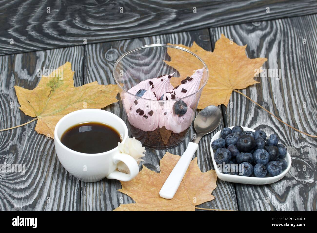 Zephyr in un bicchiere. Con biscotto e mirtilli. Accanto si trova una tazza di caffè e un piatto di mirtilli. Tra le foglie d'acero. Su tavole di pino pai Foto Stock