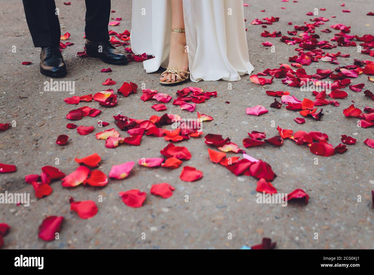 gambe e piedi di sposa e sposo con abito bianco e pantaloni neri, alcuni  petali di rosa e rosso sono sdraiati a terra Foto stock - Alamy
