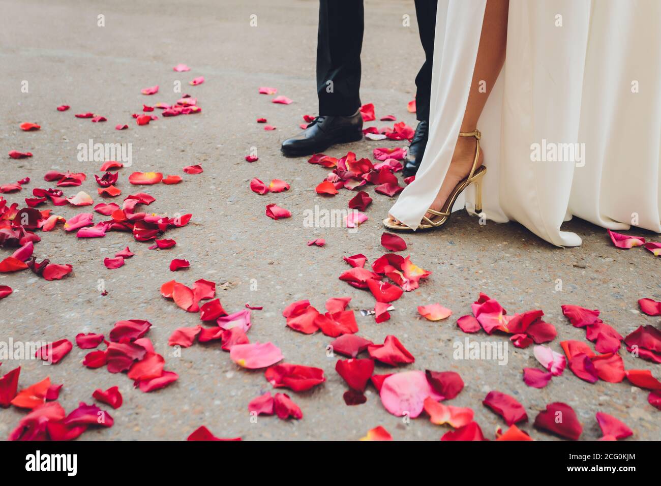 gambe e piedi di sposa e sposo con abito bianco e pantaloni neri, alcuni  petali di rosa e rosso sono sdraiati a terra Foto stock - Alamy