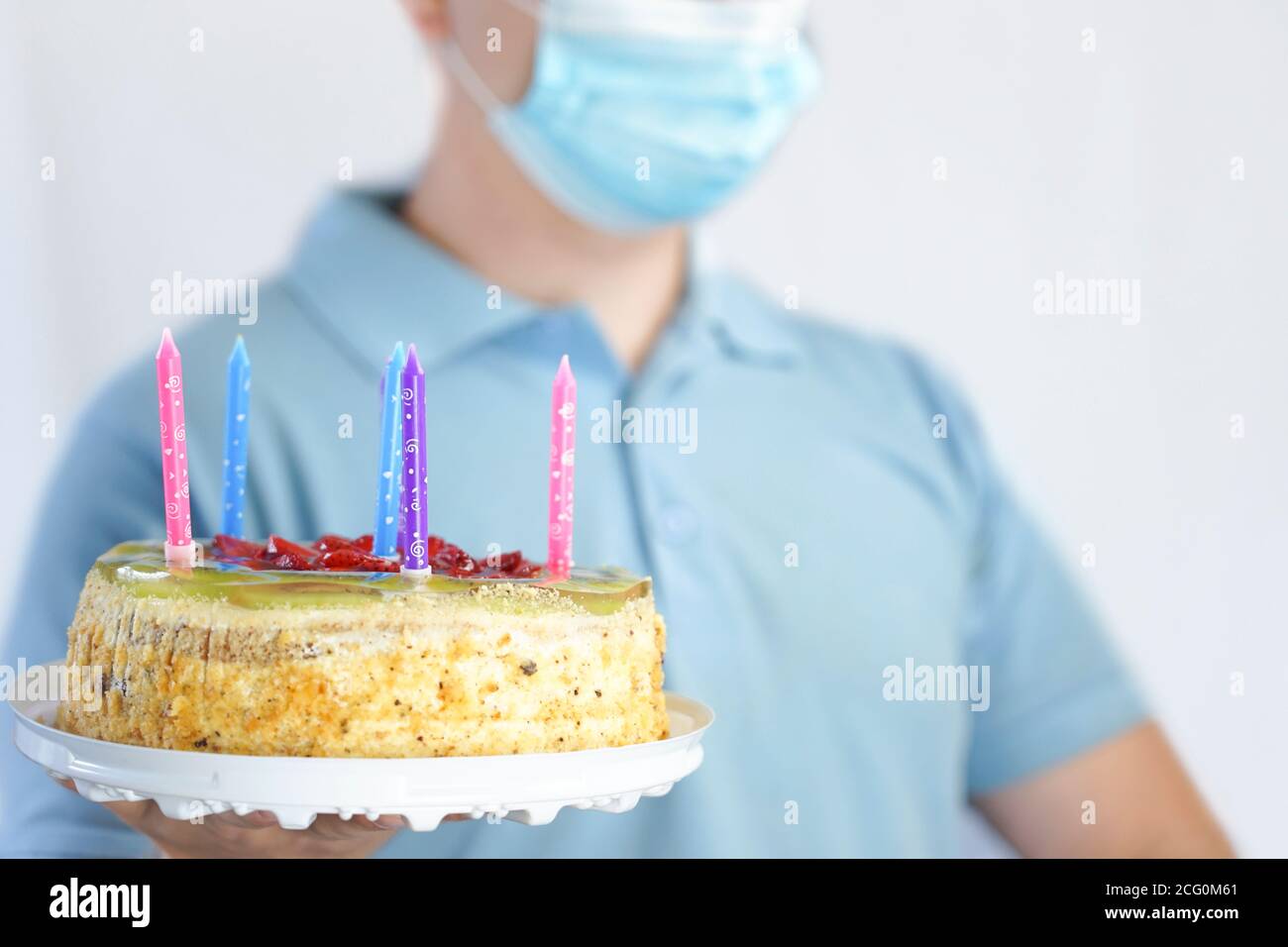 Il ragazzo nella maschera tiene una torta in mano. Festa di compleanno durante quarantena covid-19 Foto Stock