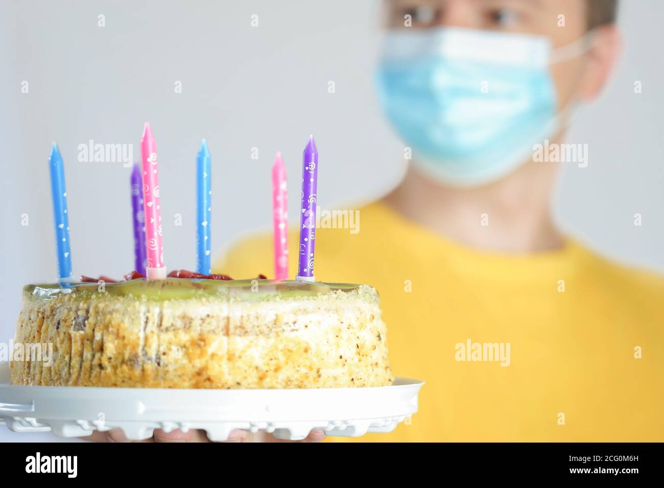 Il ragazzo nella maschera tiene una torta in mano. Festa di compleanno durante quarantena covid-19 Foto Stock