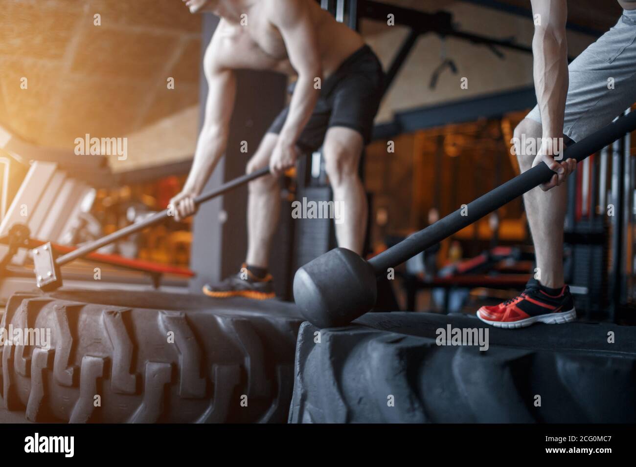 Sport Fitness uomo che colpisce ruota pneumatico con Hammer slitta Cross FIT allenamento, Young Healthy Guy Gym interno Foto Stock