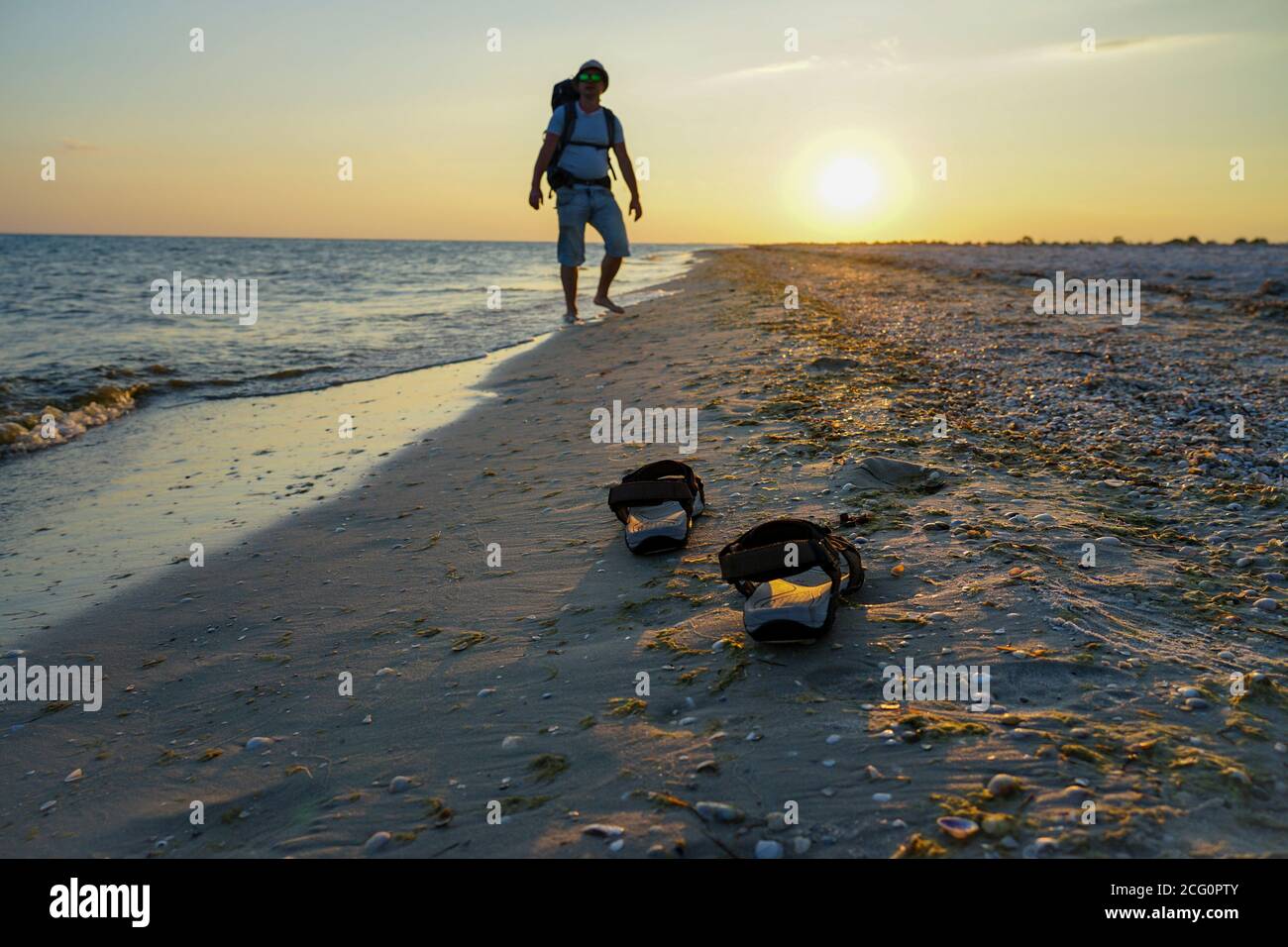 sandali su sabbia bagnata vicino al mare. Il ragazzo cammina con uno zaino  lungo la costa. I raggi del sole serale si riflettono nella sabbia bagnata  Foto stock - Alamy