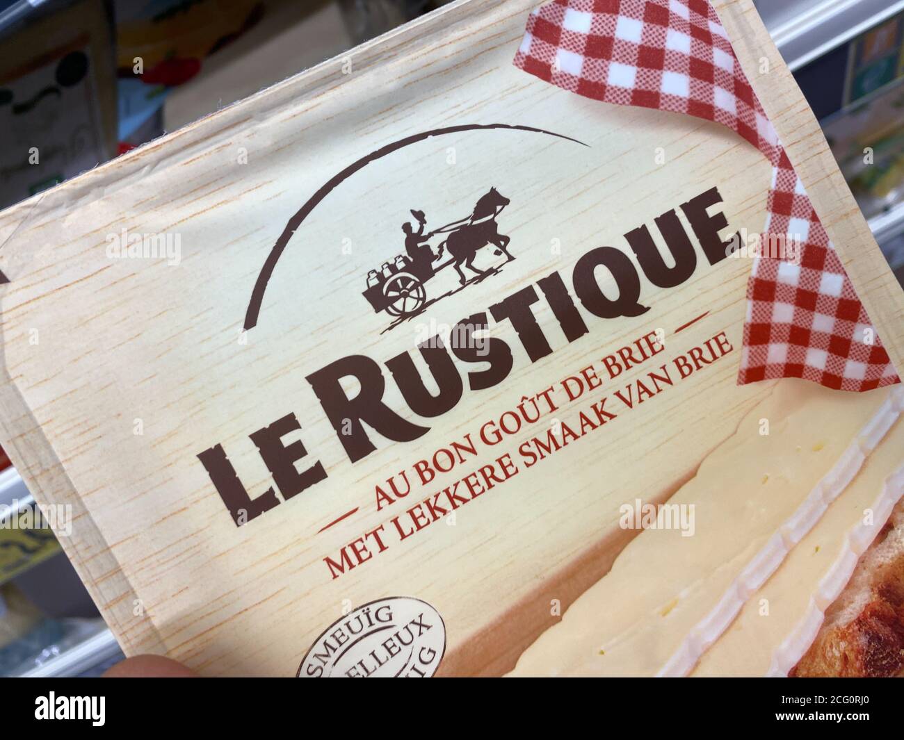 Viersen, Germania - 9 luglio. 2020: Visualizza sul pacchetto le Rustique camembert formaggio tenere a mano di fronte al ripiano in tedesco supermercato (Focus su pacchetto cen Foto Stock