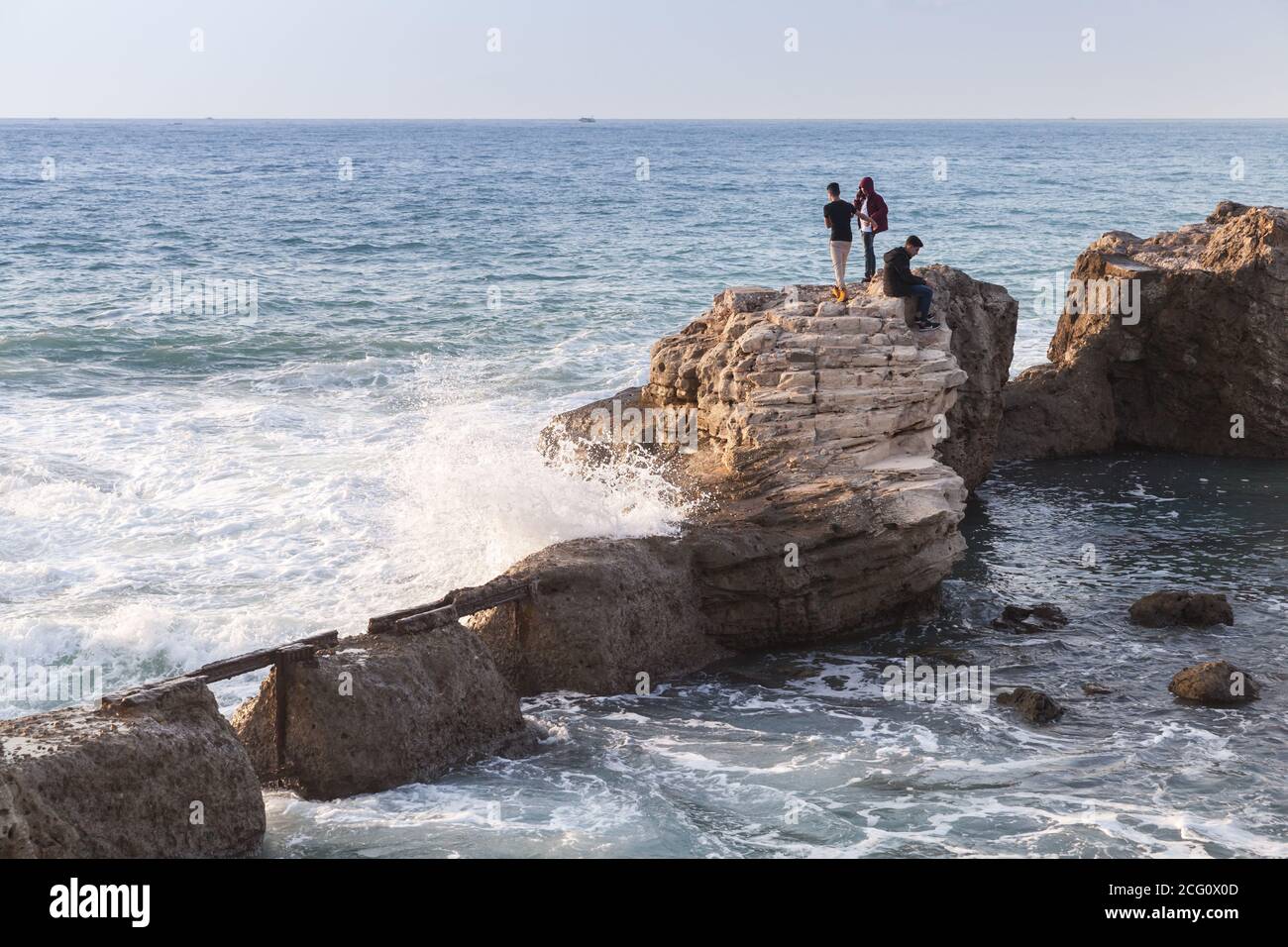Alessandria, Egitto - 13 dicembre 2018: Paesaggio con fortificazioni costiere in rovina. I ragazzi camminano sulle pietre vicino alle grandi onde che spruzzano Foto Stock