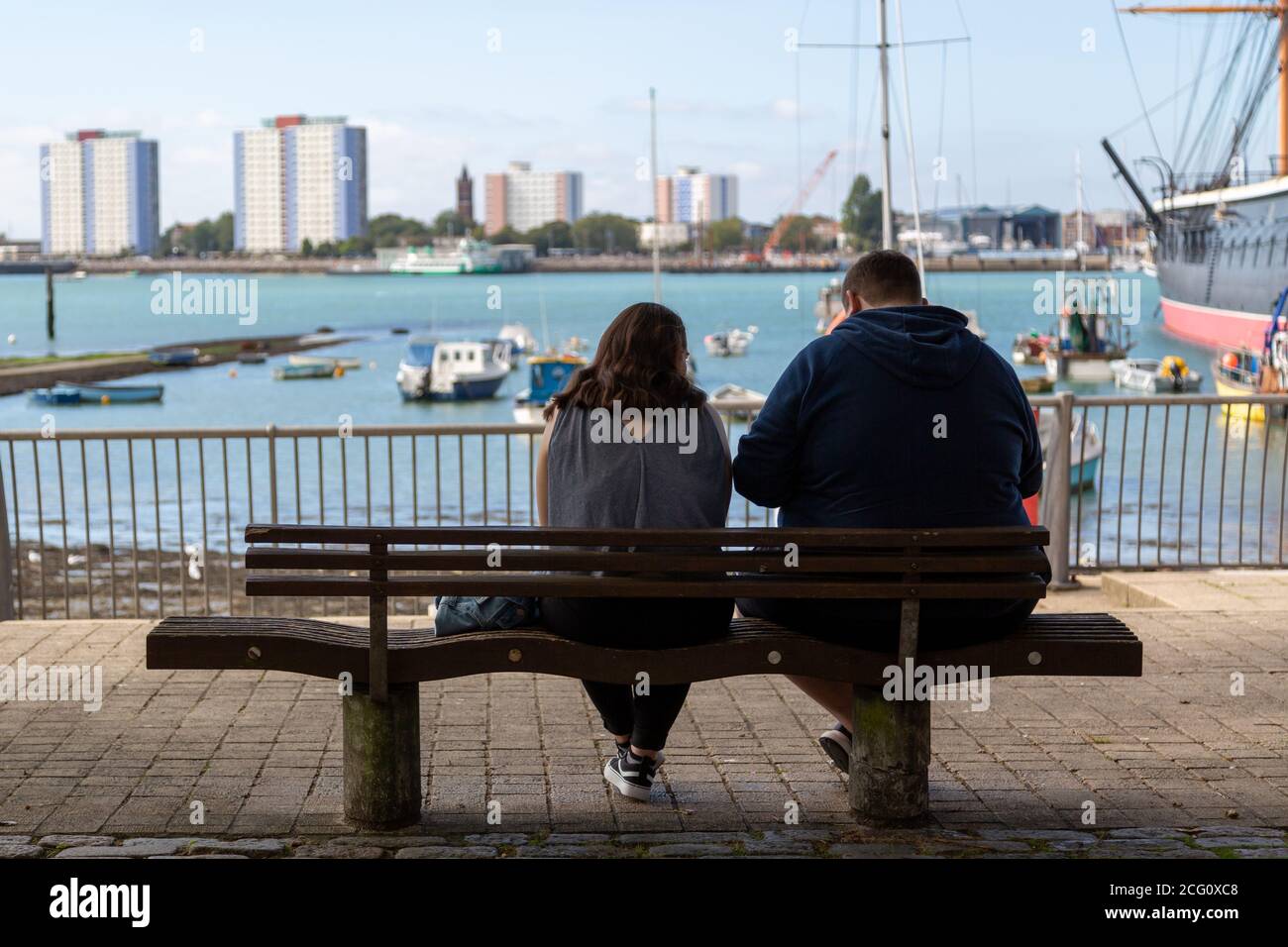 Una coppia riposante su una panchina che guarda al mare Alla vista di HMS Warrior dall'Hard in Portsmouth Foto Stock