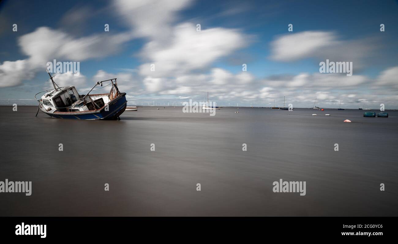 Una barca ormeggiata elenca sulla sabbia come la marea si spegne Foto Stock